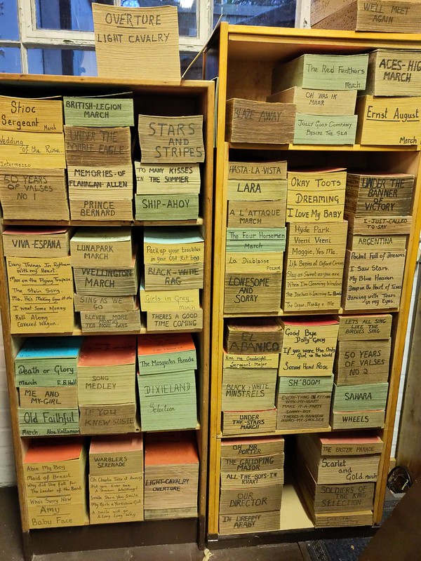 Two shelves with large stacks of paper. One the side is written the names of the pieces.