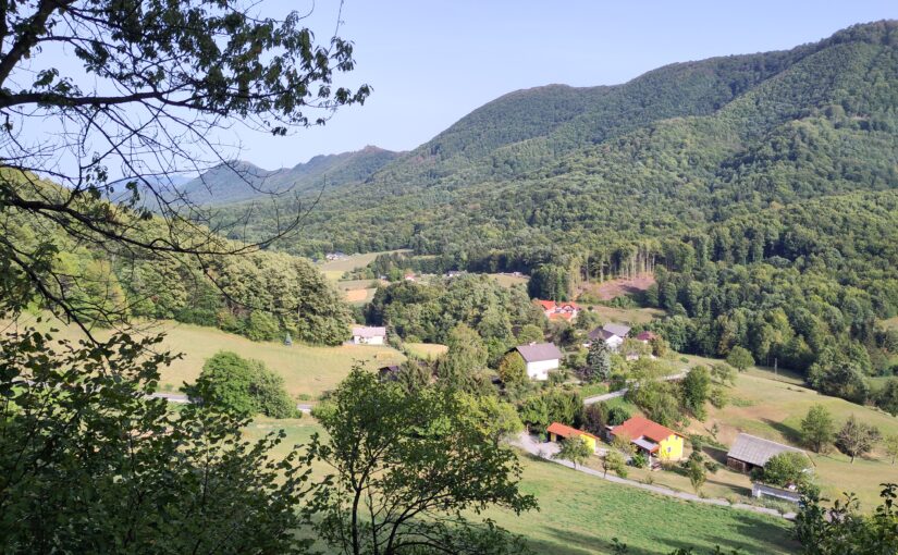 A grassy slope down to a distant village and more distant hills.